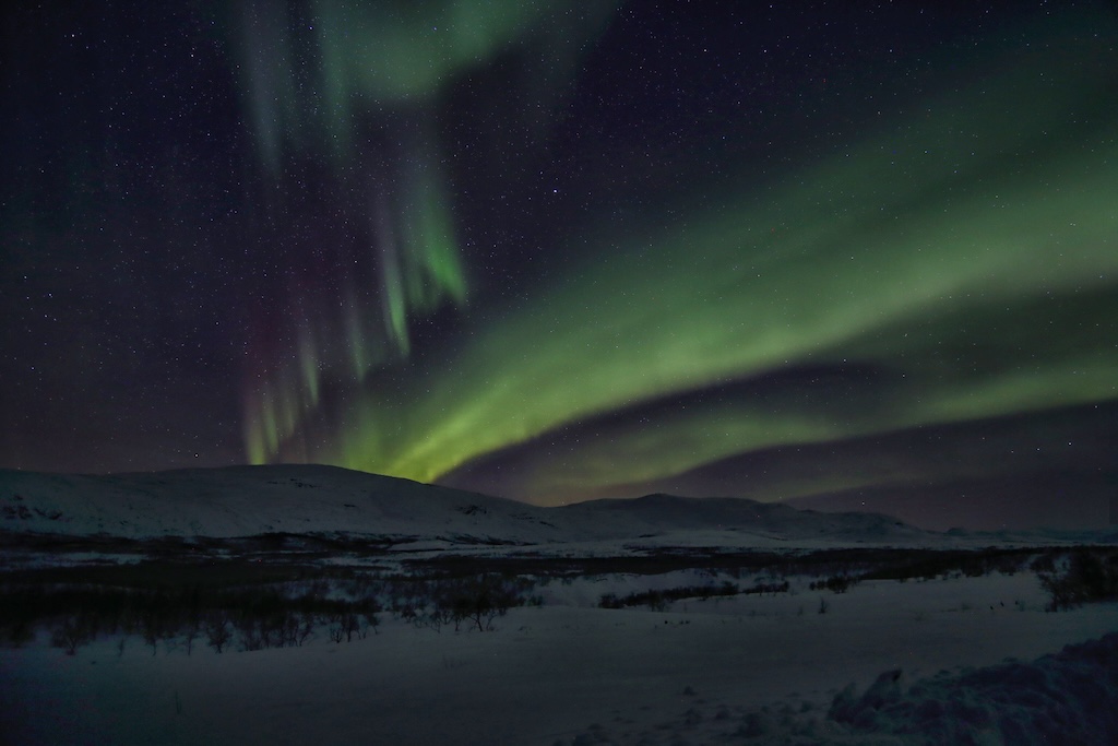 Green and violet aurora bands over snow-covered hills in Finnish Lapland