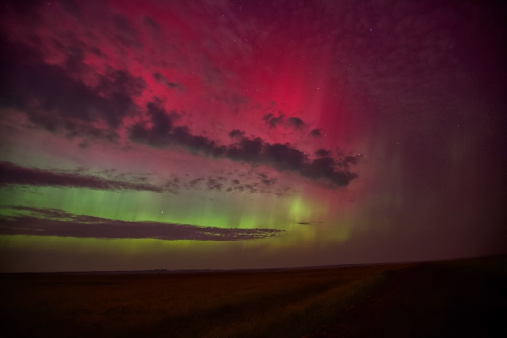 Deep red aurora above a green band, over open farmland in Montana