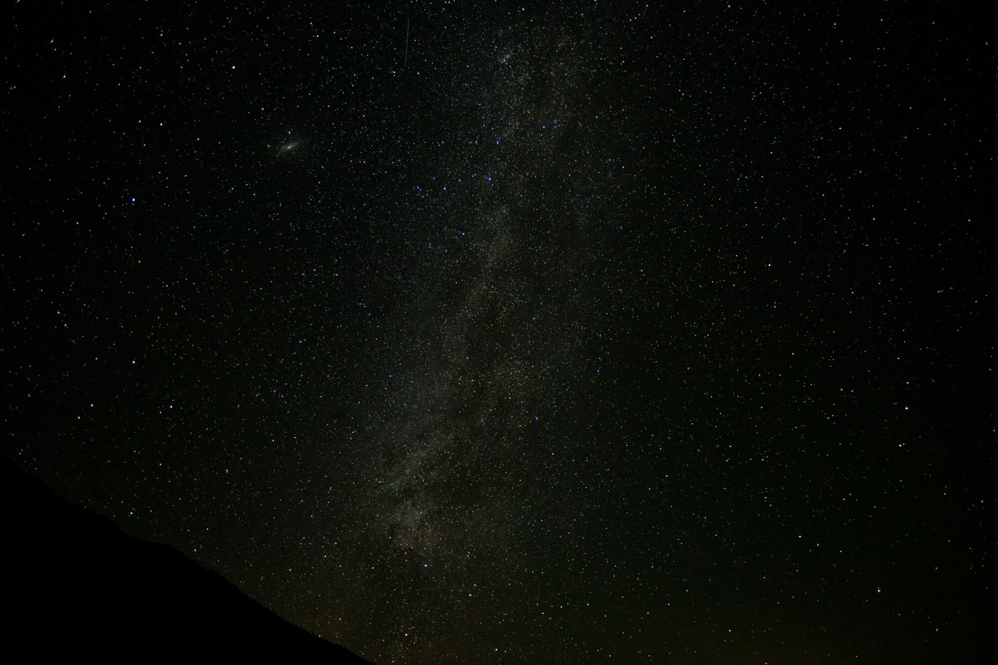 The faint oval glow of the Andromeda Galaxy in the upper left of a star-filled sky, with the Milky Way running vertically through the middle of the frame near Mono Lake.