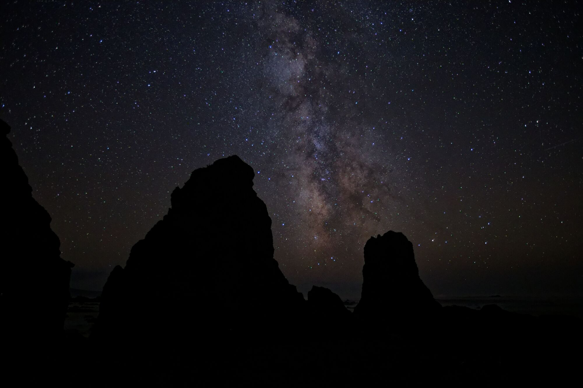 The Milky Way arching above dark sea stacks on the Lost Coast of California, with thousands of stars visible.